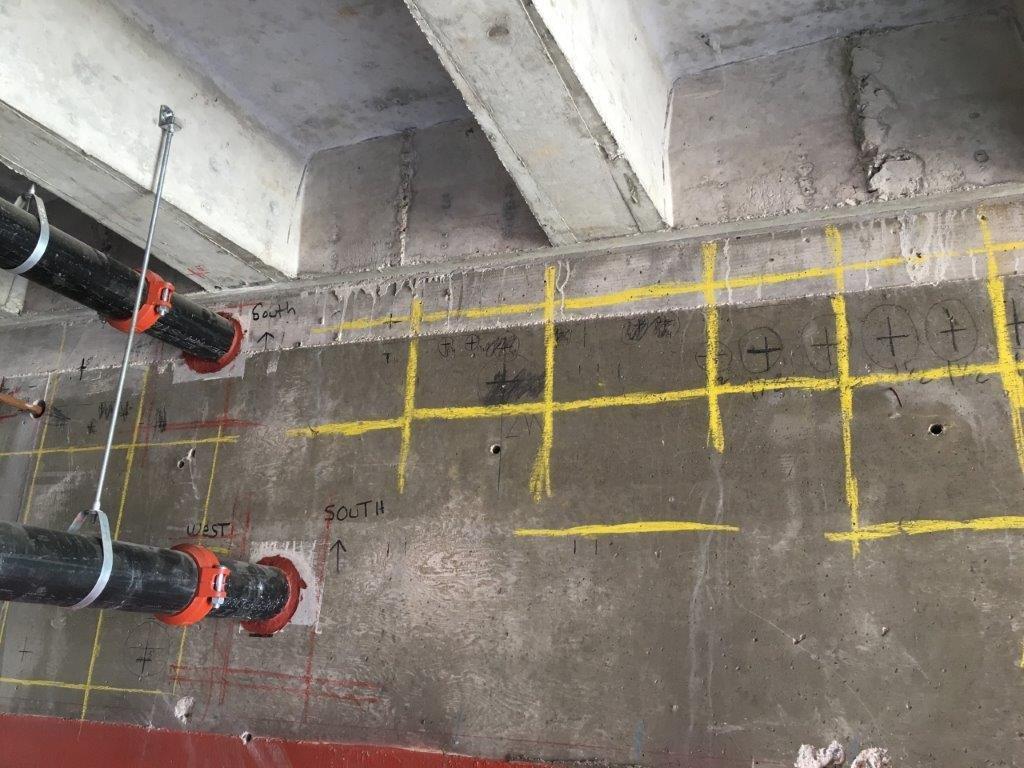 Utility locator markings on concrete around plumbing pipes.